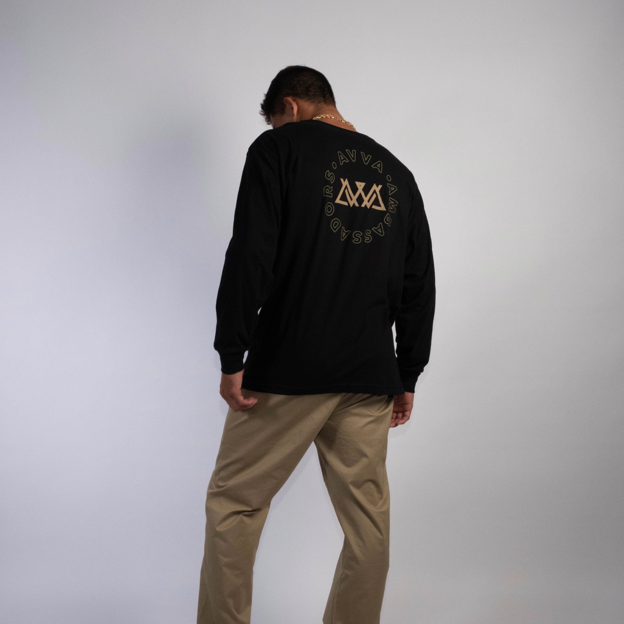 BACK VIEW OF WATERSHED LONGSLEEVE. SHOWS BACK LARGE LOGO WITH AVVA LOGO IN THE MIDDLE AND AVVA AMBASSADORS WRAPPING AROUND THE LOGO AS THE DESIGN. MODEL CASUALLY WEARING THE LONGSLEEVE LOOKING FORWARD.
