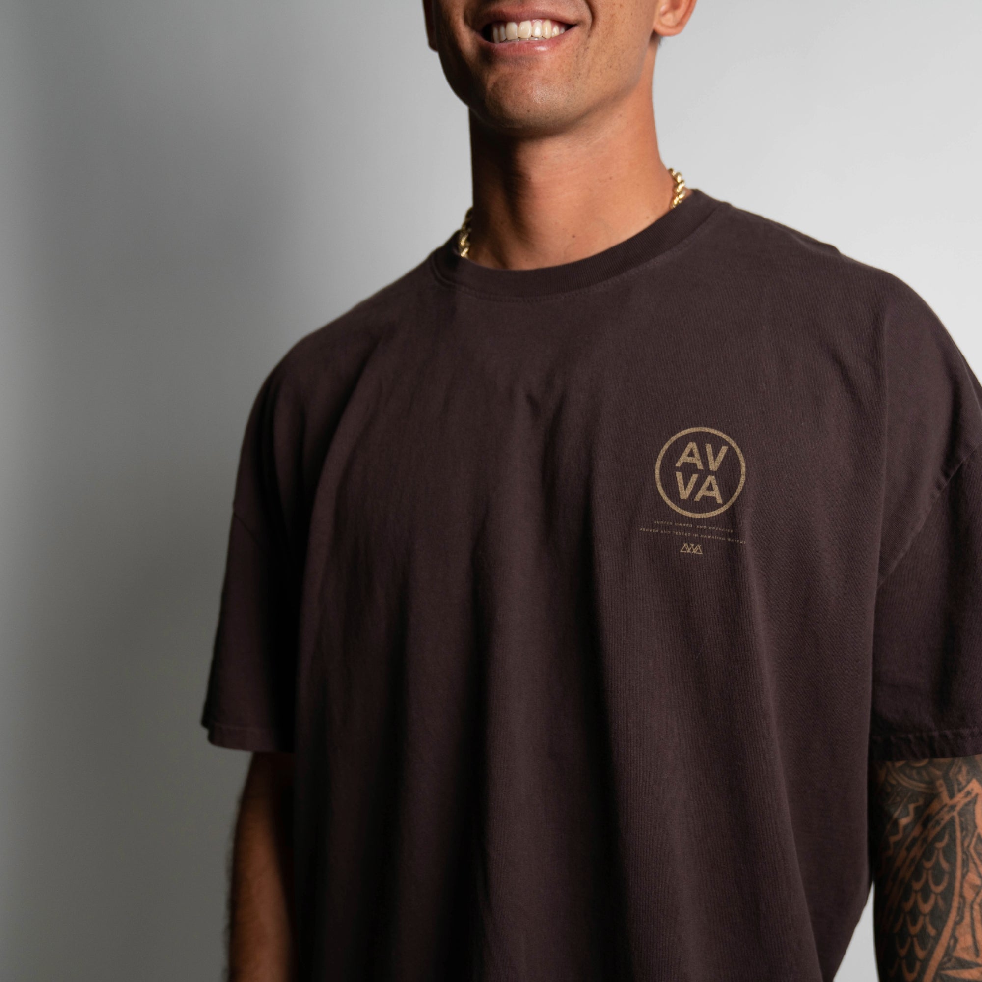 FRONT VIEW OF BROWN HEAVYWEIGHT CREED TEE ON MODEL LOOKING FORWARD. HIGHLIGHTING TOP RIGHT AVVA LOGO.