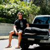 MODEL SITTING AT THE BACK OF TRUCK WEARING KILAUEA BLACK TEE