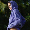 FEMALE MODEL LOOKING BACK WEARING DIAMOND HEAD PURPLE HOODIE WITH PALM TREE BACKGROUND AWITH