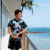 FRONT PHOTO OF THE MODEL WEARING KUHIO CRYSTAL CUSTOME DYED TEE LEANING ON A RAILING NEXT TO THE OCEAN