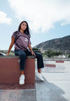 FRONT VIEW OF FEMALE MODEL SITING IN A SKATE PARK WEARING BLAKE AND BONES TEE