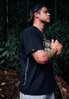 MALE MODEL WEARING COAST TO COAST BLACK TEE IN JUNGLE.