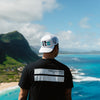 BACK VIEW OF MALE MODEL WEARING CHESTER WHITE HAT OVER LOOKING HAWAII ISLAND. ALSO WEARING CHESTER BLACK TEE.