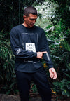 FRONT VIEW OF MALE MODEL WEARING DIESEL BLACK LONG SLEEVE IN JUNGLE POINTING TO SLEEVE PRINT DETAIL.