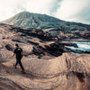 BACK VIEW OF MODEL WALKING WEARING DA BOMB BLACK TEE ATOP ROCKY MOUNTAIN IN HAWAII.