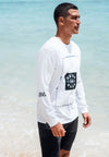 FRONT QUARTER VIEW OF MODEL WEARING DIESEL WHITE LONG SLEEVE TEE ON BEACH WITH OCEAN IN BACKGROUND