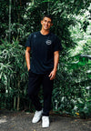 FRONT VIEW OF MODEL WEARING NIXON BLACK TEE WITH GREENERY IN BACKGROUND