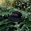 FRONT PRODUCT IMAGE OF WAIMEA HAT ON TOP OF LARGE PALM LEAVES IN THE MIDDLE OF THE JUNGLE