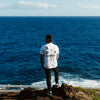 BACK VIEW OF MODEL WEARING WHITE WATER TEE LOOKING OUT TO THE OCEAN